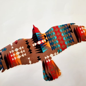 May include: A brown fabric eagle silhouette with a geometric pattern in shades of red, orange, blue, and white.