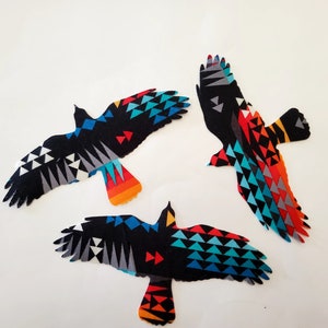 May include: Three fabric bird shapes with outstretched wings. The birds are primarily black with colorful geometric patterns in shades of blue, red, orange, and white. The birds are arranged against a white background.