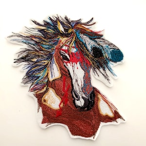 May include: Embroidered patch featuring a horse head with a colorful mane and feathers. The horse has a brown coat, white face, and red accents. The patch is outlined in white and is a unique, artistic design.