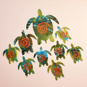 May include: A collection of nine sea turtle cutouts in varying sizes, each featuring a watercolor-style blend of green and blue hues. Every turtle displays a prominent, textured orange spiral shape centered on its shell, creating a uniform design.