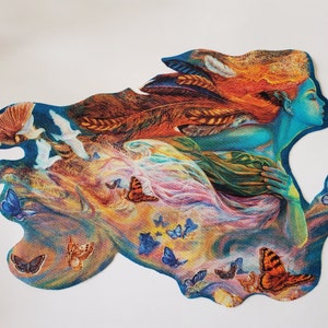 May include: A colorful illustration of a woman's profile with flowing hair and a blue complexion. The artwork features butterflies, birds, and feathers, with a vibrant mix of colors including blue, orange, and pink. The image is cut out with a unique shape.