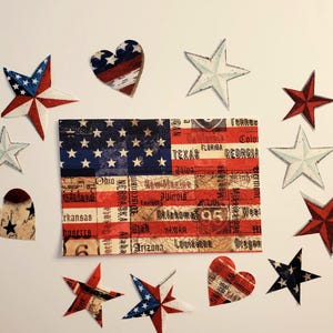 May include: An arrangement of patriotic-themed decorations. A central rectangular piece depicts the American flag with state names. Surrounding it are star and heart-shaped ornaments in red, white, and blue, evoking a sense of national pride.