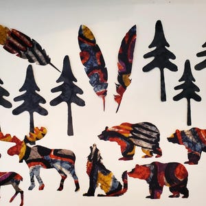 May include: A collection of fabric cutouts featuring two patterned feathers, five solid black pine tree silhouettes, a deer, a moose, a howling wolf, and two bears. The animals and feathers display a vibrant batik-style pattern in red, orange, yellow, blue, and black.