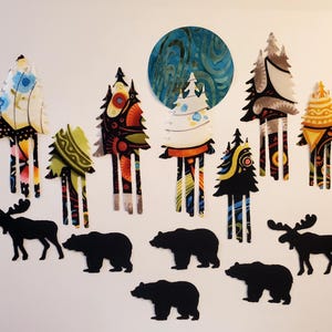 May include: A collection of paper cutouts featuring seven stylized trees with diverse colorful patterns, a large circular blue moon, and six solid black silhouettes of animals including two moose and four bears arranged on a plain surface.