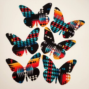 May include: A white ceramic mug with a black handle and the text "But First, Coffee" in a bold, black font. The mug is set against a blurred background, suggesting a cozy setting.