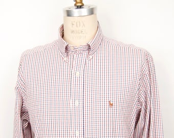 May include: A long-sleeve button-down shirt featuring a small-scale red and navy blue grid pattern on a white background. The shirt includes a button-down collar, a front button placket, and a small embroidered logo on the left chest area.