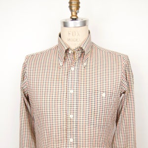 May include: A long-sleeved button-down shirt with a checkered pattern in shades of beige, brown, and blue.