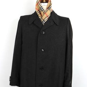 May include: A charcoal grey wool overcoat with a traditional design. It has a notched collar, button closure, and long sleeves. A plaid scarf in beige, red, and black is draped around the neck. The coat is displayed on a mannequin.