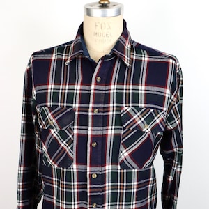 Może przedstawiać: Koszula w kratę w długim rękawem z zapięciem na guziki. Koszula jest niebieska, zielona, biała i czerwona. Ma dwie kieszenie na piersi.