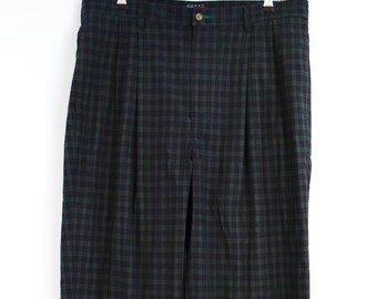 May include: A pair of pleated trousers featuring a dark green and navy blue checkered pattern. The pants include a waistband with a single button closure, a zipper fly, and belt loops. The Tommy brand label is visible on the inner waistband.