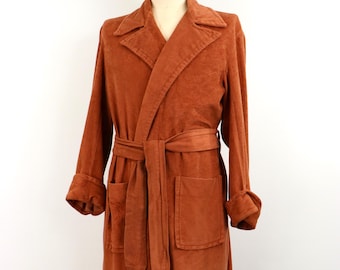 May include: A long, rust-colored robe featuring a wide collar, long sleeves with folded cuffs, and a matching tie belt at the waist. The garment includes two large patch pockets on the front and is displayed on a mannequin torso form.