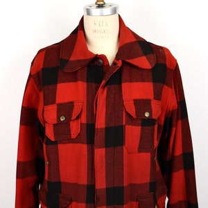 Op de afbeelding: Rood en zwart geruit flanellen jack met knoopsluiting, twee borstzakken en twee zakken aan de onderkant. Het jack heeft een kraag en lange mouwen.