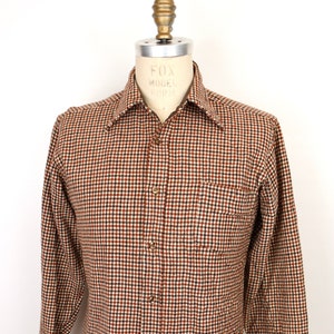 Peut inclure: Une chemise à manches longues à boutons avec un motif à carreaux brun et blanc. La chemise a une seule poche poitrine et un col boutonné.