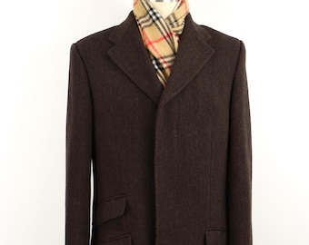 May include: A dark brown wool overcoat featuring a notched lapel, a hidden button placket, and two flap pockets on the right side with one flap pocket on the left. A beige, black, and red plaid scarf is tucked inside the collar of the coat.