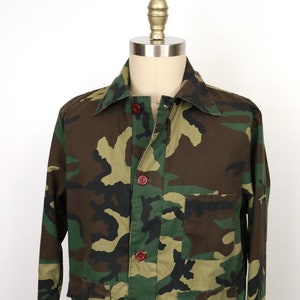 May include: A camouflage-patterned utility jacket with red buttons and multiple pockets.