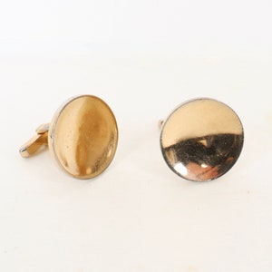 Könnte beinhalten: Ein Paar goldfarbene Manschettenknöpfe mit rundem, glattem Design.