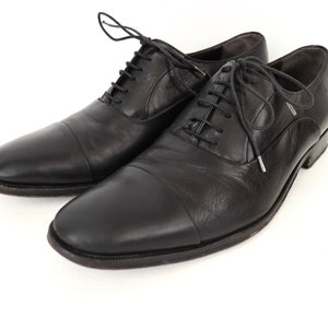 May include: A pair of black leather lace-up shoes with a cap toe design. The shoes have a classic, formal style.