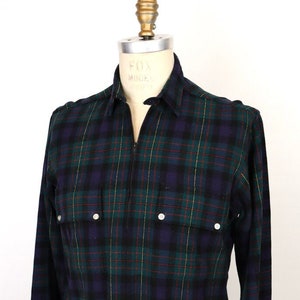 Peut inclure: Une chemise à carreaux à manches longues avec une fermeture éclair. La chemise est verte, noire et bleue avec un motif à carreaux jaunes et rouges. La chemise a deux poches à rabat avec des boutons.