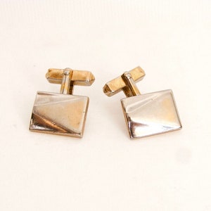 May include: A pair of vintage cufflinks with a gold-tone metal base and square, silver-tone faces. The cufflinks have a classic design, suitable for formal wear or adding a touch of elegance to any outfit.