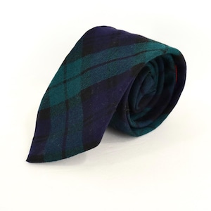 May include: A necktie featuring a dark blue and teal plaid pattern with thin black intersecting lines. The fabric has a visible woven texture, and the tie is rolled into a circular shape, displaying the pointed end and the layered folds of the material.