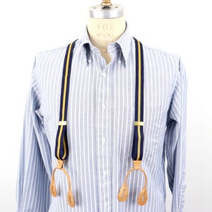 Peut inclure: Bretelles rayées bleu marine et or avec attaches en cuir, présentées sur un mannequin portant une chemise boutonnée à rayures bleu clair et blanches. Les bretelles ont un design classique.