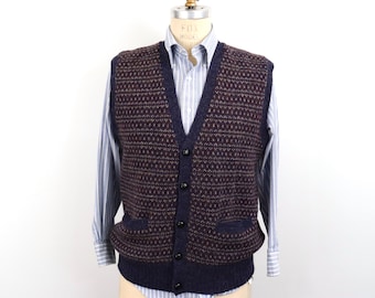May include: A dark navy blue and brown knit sweater vest featuring a repeating geometric pattern, a V-neckline, five black buttons down the front, and two front pockets, layered over a light blue and white striped long-sleeve button-down shirt.