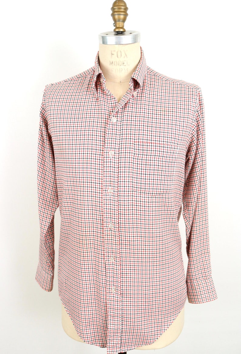 May include: A white long-sleeve button-down shirt with a red and black checkered pattern. The shirt has a single chest pocket.