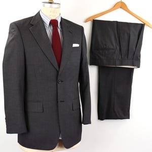 May include: A dark gray pinstripe suit with a single button closure. The jacket has a pocket on the left breast and the pants have a pleat in the front.