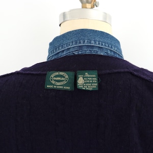 Puede incluir: Primer plano de un su&eacute;ter de lana azul marino oscuro con cuello de camisa de mezclilla. El su&eacute;ter tiene dos etiquetas verdes con texto blanco. Una etiqueta dice "Saddles San Francisco Made in Hong Kong". La otra dice "XL 100% Lambswool All Pure Wool".