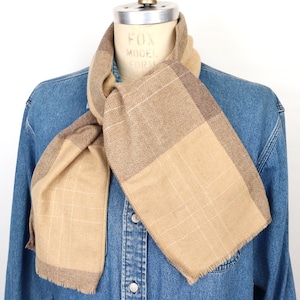 May include: A tan and brown plaid scarf with a frayed edge. The scarf is tied around a mannequin's neck.