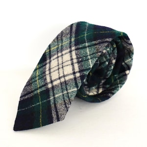 May include: A rolled-up necktie with a green, navy, white, and yellow plaid pattern. The tie is made of a textured fabric and is displayed against a white background. The plaid design features intersecting lines and squares.