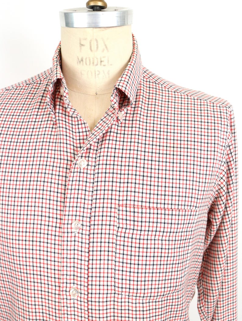 May include: A white, red, and black plaid long-sleeve button-down shirt with a single chest pocket.