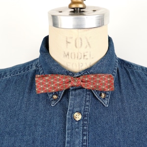 Puede incluir: Una pajarita roja y dorada con un patrón geométrico en una camisa vaquera.