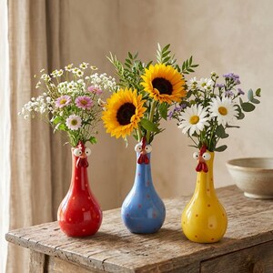 May include: Three ceramic vases shaped like chickens in red, blue, and yellow, each featuring white polka dots, a red comb, and white eyes. The vases are filled with various fresh flowers, including bright yellow sunflowers and white daisies.