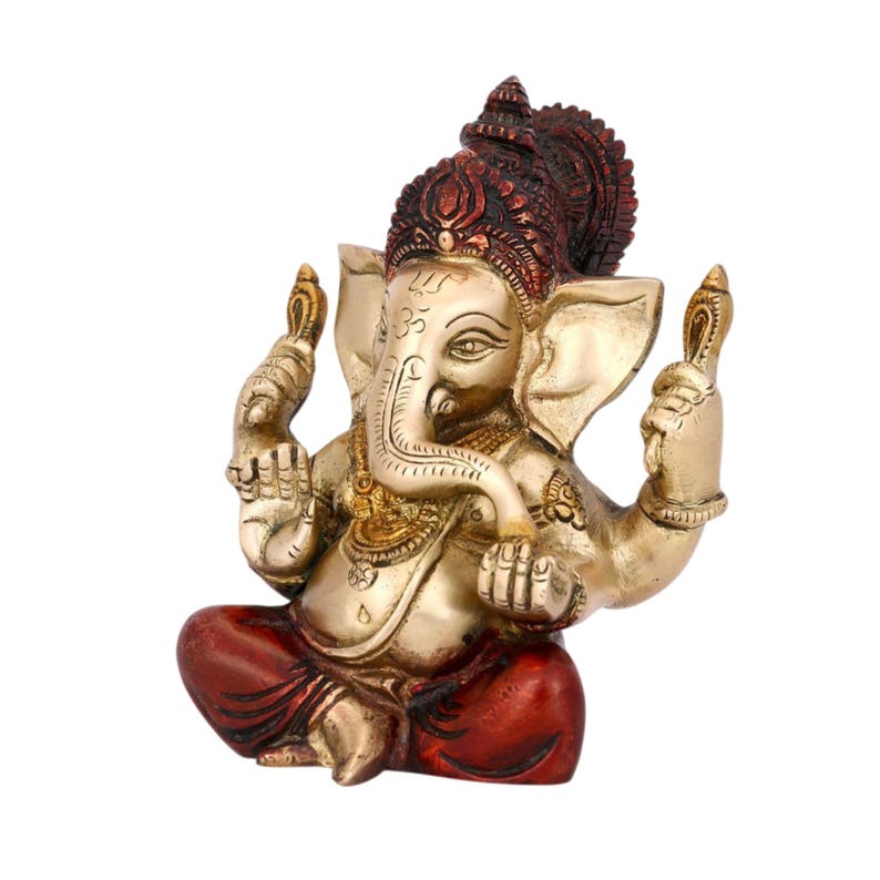 May include: A brass-colored Ganesha figurine featuring a seated posture with four arms. The deity has a prominent trunk, large ears, and a dark red headdress and lower garment. Intricate engravings adorn the body, including a symbol on the forehead.