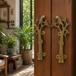 May include: A pair of antique brass door handles featuring a detailed parrot perched on a textured tree branch design. Each handle is mounted vertically onto a dark brown wooden door, showcasing intricate metalwork with visible screw holes.