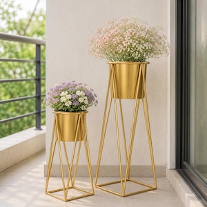 Op de afbeelding: Twee goudkleurige metalen plantenstandaards met bijpassende cilindrische potten. De hogere standaard bevat een boeket lichtroze gipskruid, terwijl de kortere standaard een arrangement van kleine paarse en witte bloemen bevat.