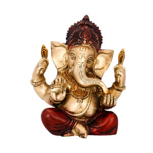 May include: A brass-colored statue of the deity Ganesha in a seated position. The figure features a prominent trunk, large ears, and four arms. It is adorned with an ornate headdress and jewelry, with deep red accents on the crown and legs.