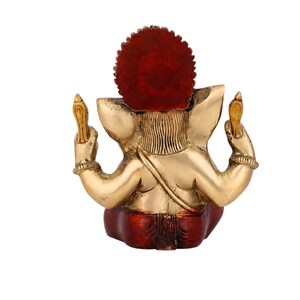 May include: A brass figurine of a deity viewed from the back, featuring a large, circular, deep red halo behind the head. The figure has metallic gold skin, raised arms holding vertical objects, and wears a deep red garment around the lower body.