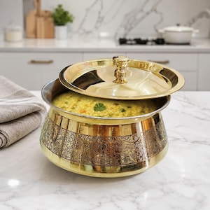 Peut inclure: Un bol de service rond en laiton avec un couvercle assorti, orné d'une gravure complexe de fleurs et de vignes sur l'extérieur. Le bol est rempli d'un plat à base de céréales jaunes contenant des petits pois verts et des morceaux de carottes.