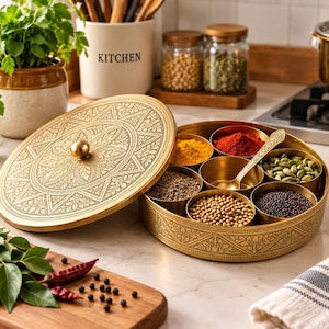 May include: A round brass spice box featuring an intricate floral engraving on the lid and side. The container includes seven small removable brass bowls filled with various colourful spices and a single brass spoon resting inside the central bowl.