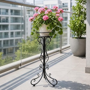 Peut inclure: Un support pour plantes en métal noir doté d'une structure haute et fine avec des volutes décoratives et un anneau supérieur circulaire. Un pot en céramique blanche texturée repose sur le support, contenant une plante verte aux fleurs roses.