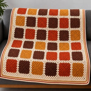 May include: A handmade crochet blanket featuring a repeating granny square pattern in shades of dark brown, burnt orange, and mustard yellow. The squares are joined by a cream-colored yarn border, and the edges are finished with a matching trim.