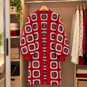 May include: A long-sleeved open-front cardigan made of crocheted granny squares in a repeating pattern of red, white, and dark grey. The garment features a solid red ribbed trim along the cuffs and the front opening, with a loose, relaxed fit.