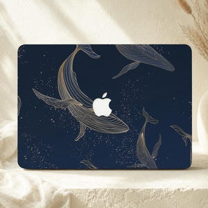 May include: A dark navy blue laptop skin featuring a gold-toned line art pattern of multiple whales swimming amidst a field of small white dots. The design incorporates the central Apple logo cutout, which remains visible as a bright white shape.