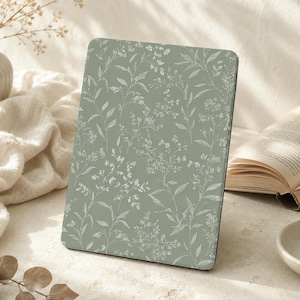 Puede incluir: Una funda rectangular para tableta o lector electrónico con fondo verde salvia y un delicado patrón botánico de líneas blancas de diversas flores silvestres, hojas y tallos que cubren toda la superficie frontal en un diseño repetitivo.