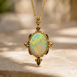 May include: A gold pendant necklace featuring an oval-shaped opal gemstone with iridescent flashes of green, yellow, and orange. The opal is set in an ornate gold frame with decorative scrollwork details and hangs from a delicate gold chain.