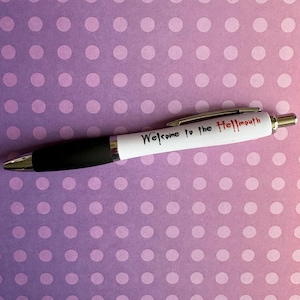 May include: A retractable ballpoint pen with a white barrel featuring the black and red text Welcome to the Hellmouth. The pen has a black rubberised grip section, a silver metal pocket clip, and a silver metal tip and end cap.