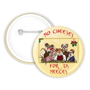 May include: A round pin-back button featuring a cream-coloured background with a central illustration of five mice in historical clothing. The text "NO CHEESES FOR US MEECES" is printed in red above and below the illustration, which includes holly.