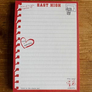 May include: A rectangular notepad with a red border and white lined paper. The top features the text EAST HIGH and a basketball hoop. It includes the phrases We're all in this together, Troy 4 Gabriella, What team?, Wildcats!, and Stick to the status quo.